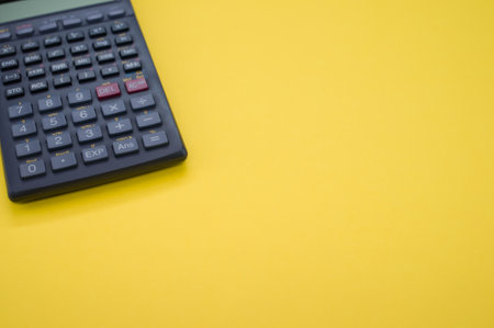 A closeup of a calculator on a yellow surface under the lightsの写真素材
