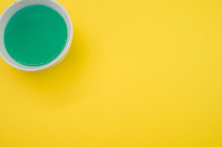 A bowl of green paint on a yellow surface with copyspaceの写真素材