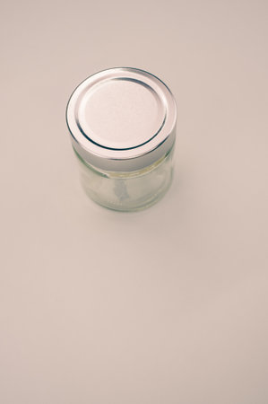 A vertical shot of a small glass jar with a cap on a light brown surfacの写真素材