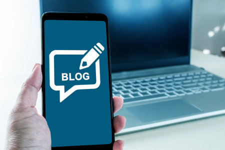 A hand holding a cell phone with a blog icon on the screenの写真素材