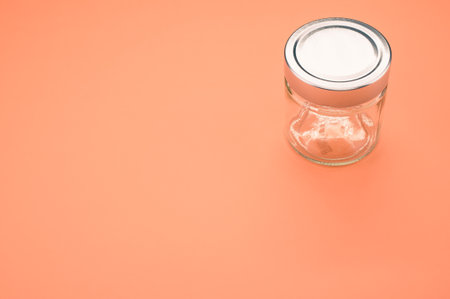 A closeup of a small glass jar with a cap on an orange surfaceの写真素材