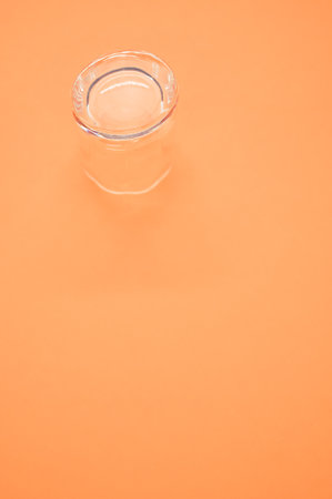 A vertical shot of a shot glass under the lights isolated on an orange backgroundの写真素材