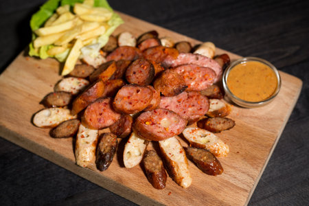 A closeup of sliced sausage and bread served with fries and sauce on a wooden plateの写真素材