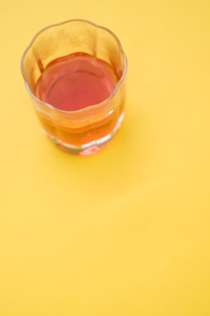 A vertical shot of a glass with red liquid on a yellow surfaceの写真素材