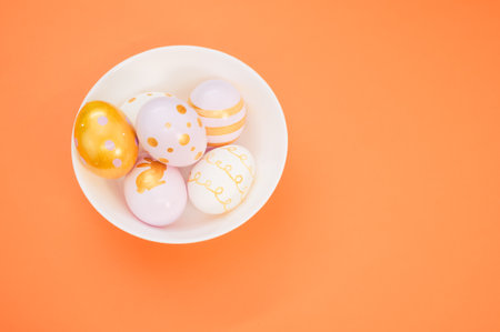 A high angle shot of a bowl of decorated eggs for Easter on an orange surfaceの写真素材