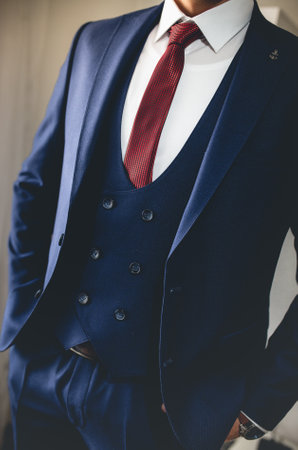 A vertical shot of a handsome groomsman in a navy suit and red tieの写真素材