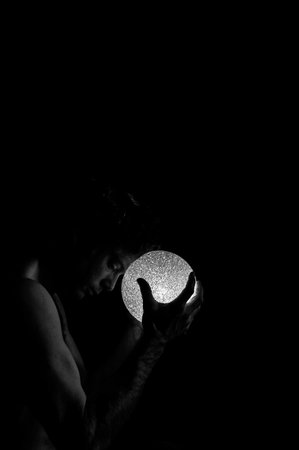 A vertical shot of a topless male holding a white light ball on a black background