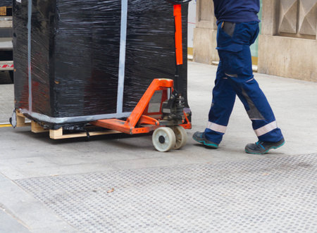 A worker with fork pallet truck stacker in warehouse loading furniture panelsの写真素材