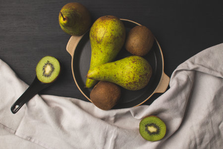 A top view of delicious ripe kiwis and pears on a tray on the table with a tablecloth on itの写真素材