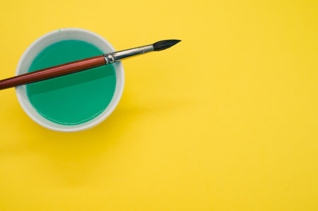A white container with green liquid paint and a paintbrush on a yellow surface - copy spaceの写真素材