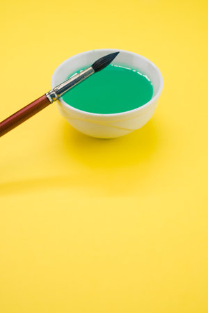 A white container with green liquid paint and a paintbrush on a yellow surface - copy spaceの写真素材