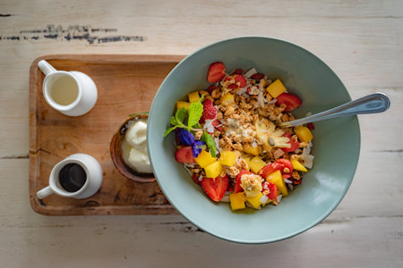 A top view of a bowl of porridge mixed with fruits served with yogurt and natural honey on a wooden trayの写真素材