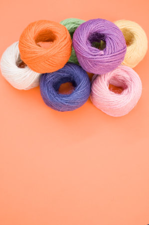 A top view of multi-colored yarn balls in the peach color background with copy space in the bottomの写真素材