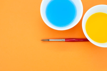 Liquid watercolor paints and paintbrush on orange background with space for textの写真素材