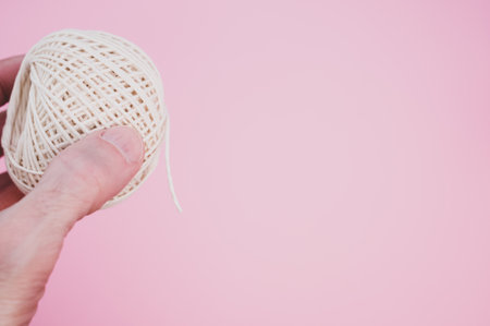 A male hand holding a beige knitting yarn in the pink background with a copy spaceの写真素材