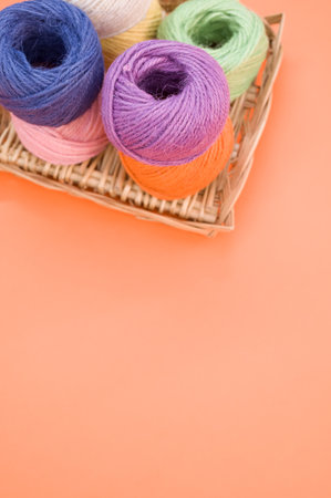 A vertical shot of colorful yarns on an orange background with space for text