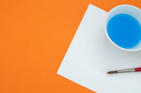 A top view of blue liquid watercolor and paintbrush on orange background with space for textの写真素材