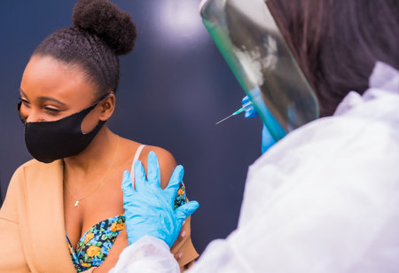 An African-American young female receiving the injection of vaccine by a doctor