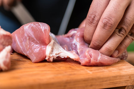 a closeup shot of hands cutting the raw meat with a sharp knifeの写真素材