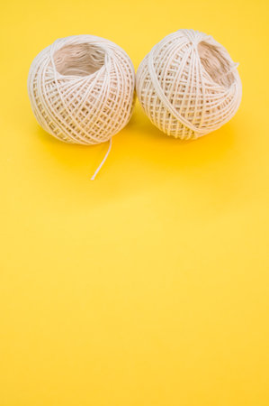A vertical shot of two white balls of twine isolated on a yellow backgroundの写真素材