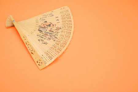 A vintage wooden hand fan with floral patterns isolated on an orange backgroundの写真素材