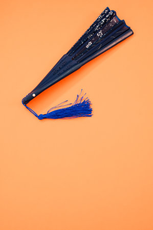 A vertical shot of a blue hand fan with floral patterns isolated on an orange backgroundの写真素材