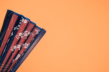 A blue hand fan with floral patterns isolated on an orange background