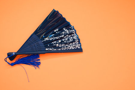 A blue hand fan with floral patterns isolated on an orangeの写真素材