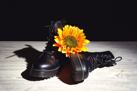 A yellow flower on leather black boots on a wooden surface