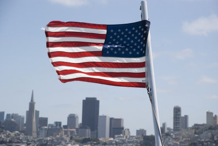 USA: American Flag waving in wind over San Francisco skyline, Californiaの写真素材