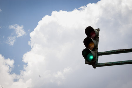 A low-angle shot of the traffic lights showing the green color against the cloudy skyの写真素材