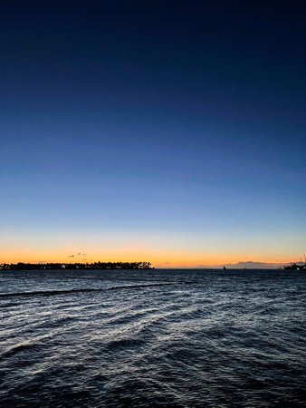 A mesmerizing scenery of a partially rough sea under a clear blue sunset sky