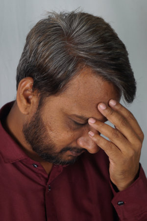 A portrait of a disappointed adult South Asian man with graying hair against a gray wallの写真素材