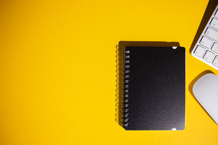 A top view of a notepad, keyboard and a mouse on a yellow work tableの写真素材
