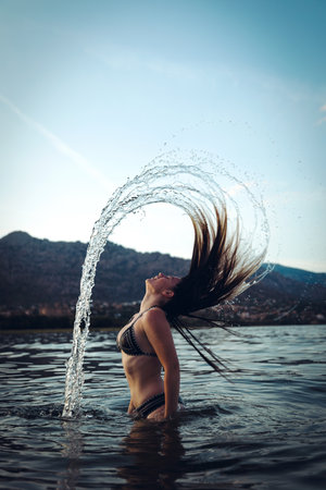 A vertical shot of a young female whipping her wet hair back in the seaの写真素材