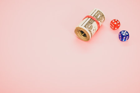 A closeup of a roll of dollars and dice isolated on pink background for a copy spaceの写真素材
