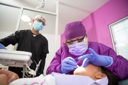 A Mexican female dentist doing dental treatment on a young girl while the male assistant is watchingの写真素材
