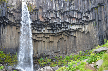 A small waterfall from a cliff with green plants on the down platoの写真素材