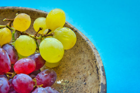 Colorful table grapes in a vintage bowl on blue background. Close-up and detail.の写真素材