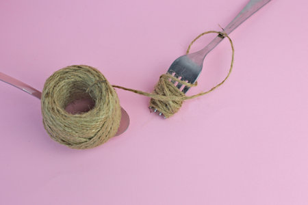 A fork and spoon with a twine rope on a pink background