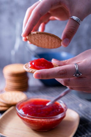 A vertical shot of hands making fresh Maria cookie (galletas Maria) with strawberry jamの写真素材