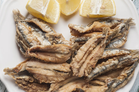 A high angle shot of fried anchovies with sliced lemons on a plateの写真素材