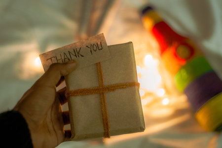 A hand holding a wrapped gift box and a note "THANK YOU" in the blurred festive backgroundの写真素材