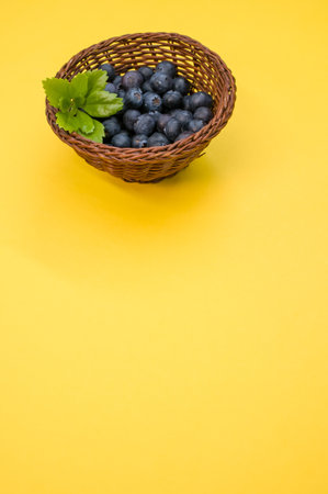 A closeup shot of blueberries in a basket on a yellow backgroundの写真素材