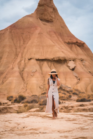 A brunette Caucasian girl with an explorer outfit with a white dress walking enjoying the desert of Las Bardenas Reales in Navarra. Spainの写真素材