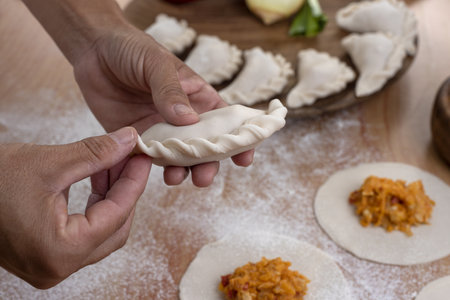 A person making Argentinian empanadas stuffed with vegetables and squash on wooden surfaceの写真素材