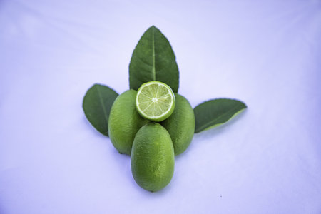 A closeup of fresh limes with leaves on a light purple surfaceの写真素材