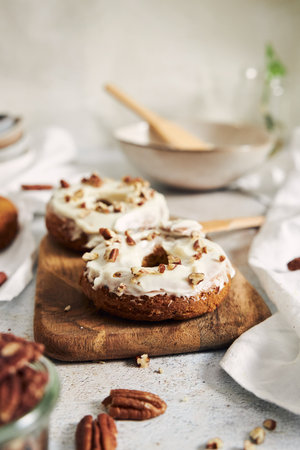 A vertical shot of delicious carrot pastries donuts with cream and nuts on top on a tableの写真素材