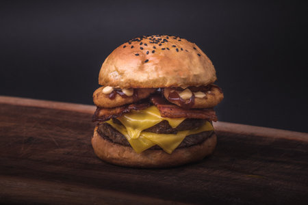 A closeup of a fresh double cheeseburger with onion rings and sauce on a wooden boardの写真素材