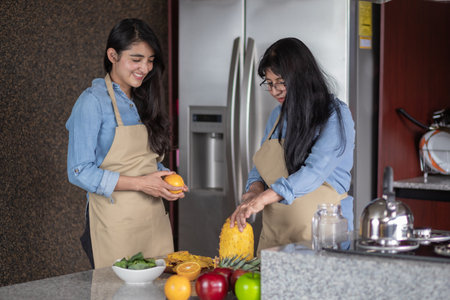 A happy Mexican mother and daughter cutting fruits in the kitchenの写真素材